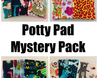 Könnte beinhalten: Ein Set mit sechs bunten und gemusterten Töpfchenunterlagen. Die Unterlagen sind aus weichem Fleece und haben verschiedene Designs, darunter Tiere, Blumen und geometrische Muster. Die Unterlagen sind mit "Potty Pad Mystery Pack" beschriftet.
