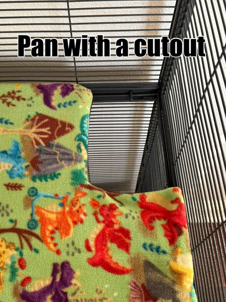 K&ouml;nnte beinhalten: Eine Fleece-K&auml;figeinlage mit hellgr&uuml;nem Hintergrund und einem bunten Muster aus Drachen und B&auml;umen, passend f&uuml;r eine Wanne mit Ausschnitt. Der Stoff liegt in einem schwarzen Drahtk&auml;fig. Der Text Pan with a cutout ist zu sehen.