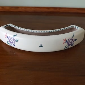 Könnte beinhalten: Ein weißer Keramik-Pflanztopf mit braunem Innenraum und einer geschwungenen Form. Er hat eine grüne und weiße Punktlinie am Rand und zwei Blumendesigns mit violetten, rosa und grünen Akzenten.