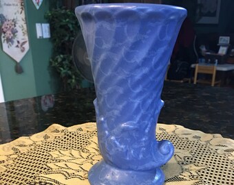 May include: A blue ceramic vase with a swirl design. The vase is sitting on a lace doily.