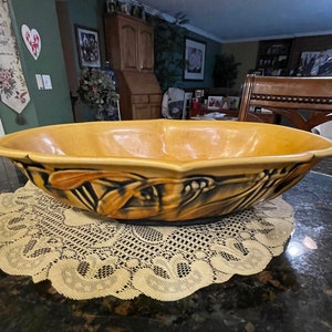 May include: A large, yellow ceramic bowl with a brown and black floral design. The bowl is sitting on a white lace doily.