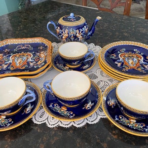 May include: A blue and gold tea set with a teapot, cups, saucers, and a square plate. The set features a decorative design with a coat of arms and floral motifs.