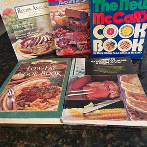 May include: A collection of vintage cookbooks, including "Sunset Recipe Annual 1996 Edition," "Weight Watchers Favorite Recipe," and "The New McCall's Cook Book." The books feature colorful covers with images of food and recipes.