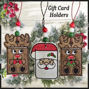 May include: Embroidered Christmas gift card holders featuring a reindeer and Santa Claus design. Each holder is brown, white, and red, with a beaded string for hanging. The text "Gift Card Holders" is visible.