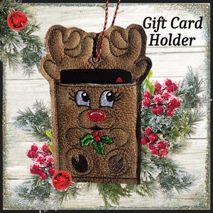 May include: Brown reindeer gift card holder with embroidered details, including a red nose and holly. The holder has a pocket for a gift card and is decorated with Christmas greenery and ornaments. Text on the image reads "Gift Card Holder."
