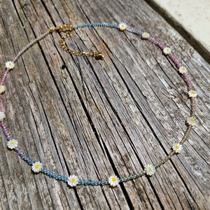 May include: A delicate necklace with a gradient of blue, pink, and white beads. Each bead is adorned with a small white daisy charm.