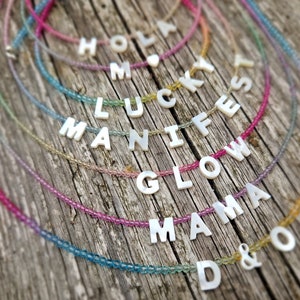 May include: A set of colorful beaded necklaces with white letter charms spelling out the words "Hola", "Mama", "Glow", "Manifest", "Lucky", and "D&O".