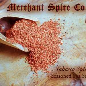 May include: A wooden scoop filled with red and orange Tabasco Spicy Sea Salt from the Merchant Spice Co. Seasoned Sea Salt Collection.