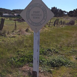 Peut inclure: Un panneau blanc avec le mot "MALDON" en lettres noires. En dessous du panneau se trouve un panneau brun en forme de losange avec le texte "National Trust of Australia, First Notable Town, Victoria".