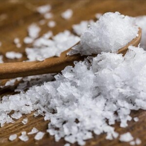 Peut inclure: Une cuill&egrave;re en bois remplie de cristaux de sel marin blanc, avec plus de sel &eacute;parpill&eacute; autour sur une surface en bois brun.