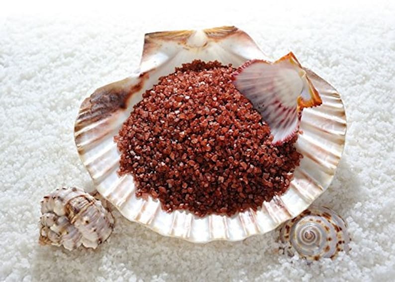 May include: Red sea salt in a seashell, with a smaller seashell on the white sand.