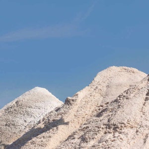 May include: A row of white salt mounds against a clear blue sky. The mounds are different sizes and shapes, creating a unique and interesting landscape.