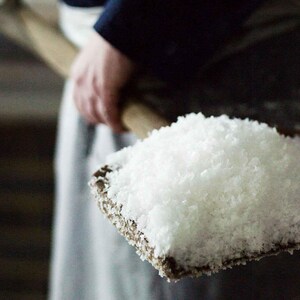 Peut inclure: Une personne tenant une pelle en bois remplie de cristaux de sel blanc.
