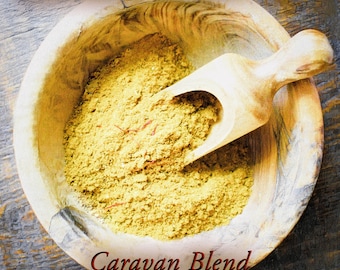 May include: A wooden bowl filled with a yellow spice blend, labeled "Caravan Blend" and "Fanciful Collection". A wooden scoop is partially submerged in the spice.