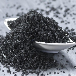 May include: A close-up of black Hawaiian salt in a white bowl. The salt is coarse and has a dark, almost black color.