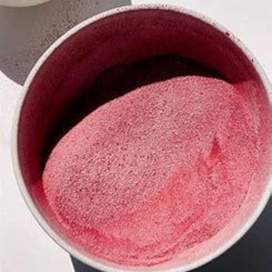 May include: A close-up shot of a white bowl filled with pink powder, possibly a food ingredient. The bowl is set against a white surface, with a smaller bowl of red berries visible in the upper left corner. The lighting creates shadows.