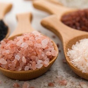 May include: Five wooden spoons filled with different types of salt: black salt, pink Himalayan salt, red salt, and two types of white salt.