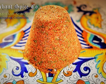 May include: A mound of orange and green Hungarian seasoning in a white bowl with a blue and yellow floral design. The seasoning is labeled "Merchant Spice Co. Hungarian Seasoning European Collection."