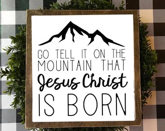 Puede incluir: Un letrero de madera blanco con texto negro y una silueta de montaña. El texto dice "Go tell it on the mountain that Jesus Christ is born."