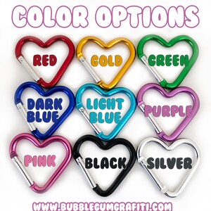 May include: Nine heart-shaped carabiners in different colors: red, gold, green, dark blue, light blue, purple, pink, black, and silver.  The carabiners are arranged in three rows of three.  The text "COLOR OPTIONS" is at the top of the image.  The text "www.bubblegumgrafiti.com" is at the bottom of the image.