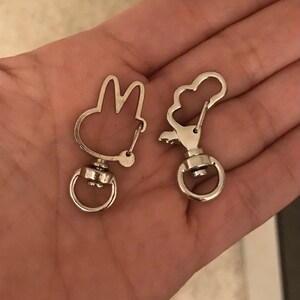 May include: Two silver keychains, one shaped like a bunny rabbit and the other shaped like a cloud. Both keychains have a silver swivel clasp.