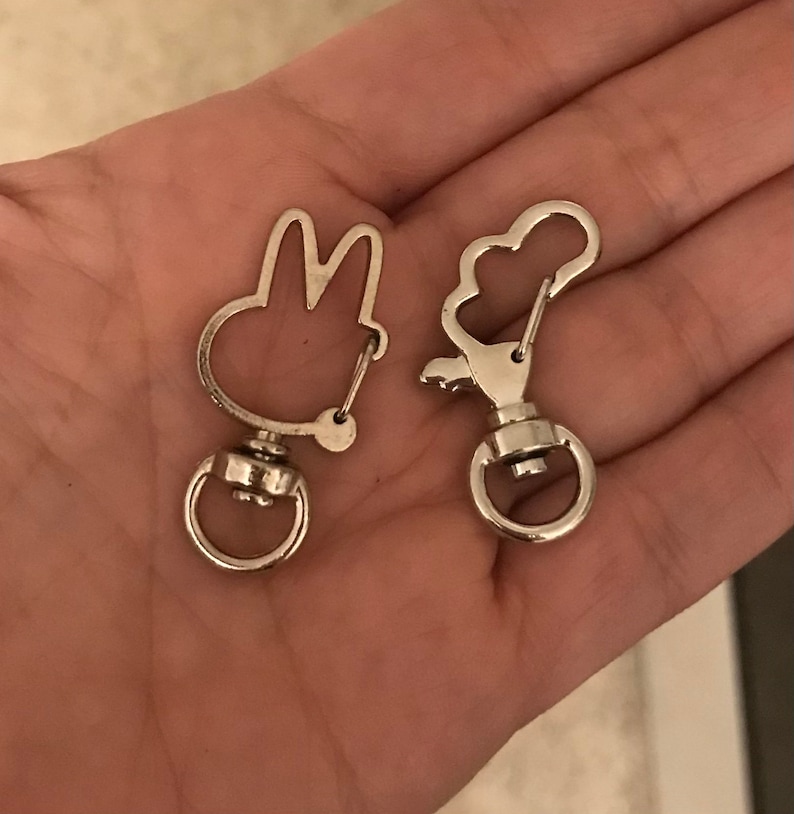May include: Two silver keychains, one shaped like a bunny rabbit and the other shaped like a cloud. Both keychains have a silver swivel clasp.