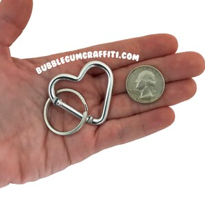 May include: Silver heart-shaped carabiner keychain with a silver key ring. The keychain is about the size of a US quarter.