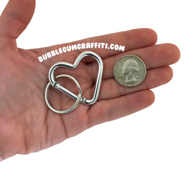 May include: Silver heart-shaped carabiner keychain with a silver key ring. The keychain is about the size of a US quarter.