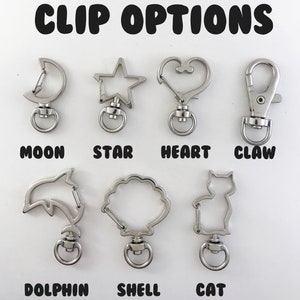 May include: A set of 9 silver metal keychains with different shapes, including a moon, star, heart, claw, dolphin, shell, and cat. The keychains are labeled with their corresponding shapes.