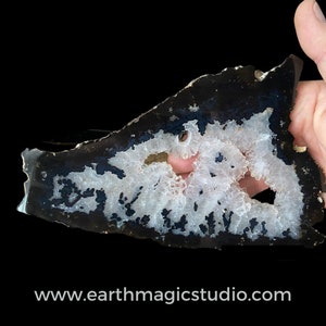 May include: A large, irregularly shaped slice of agate with a black and white pattern. The agate has a natural, rough edge and a smooth, polished surface. The white areas of the agate are filled with small, white crystals.