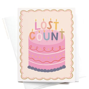 May include: A birthday card with a pink cake design. The cake has candles spelling "LOST COUNT". The card has a scalloped border and is accompanied by a white envelope.