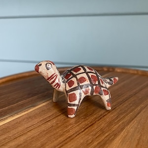 May include: A white ceramic mug with a black handle and the text "But First, Coffee" in a bold, black font. The mug is set against a blurred background, suggesting a cozy setting.
