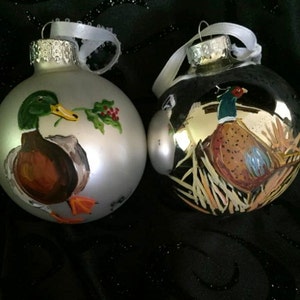 May include: Two hand-painted Christmas ornaments, one silver with a mallard duck and holly, the other silver with a pheasant.