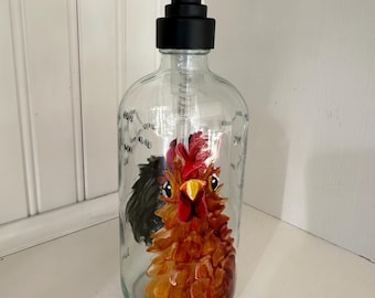 May include: A glass soap dispenser with a black pump top and a hand-painted rooster design. The rooster is brown, red, and yellow with a black wing.