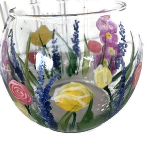 May include: A clear glass bowl with a hand-painted floral design. The flowers are yellow, pink, and purple, and they are painted in a realistic style. The bowl is perfect for displaying flowers or candles.