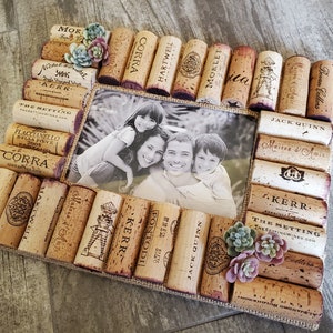 Puede incluir: Un marco de fotos hecho de corchos de vino, con una foto en blanco y negro de una familia de cuatro personas en su interior. El marco est&aacute; decorado con peque&ntilde;as suculentas verdes y rosas.