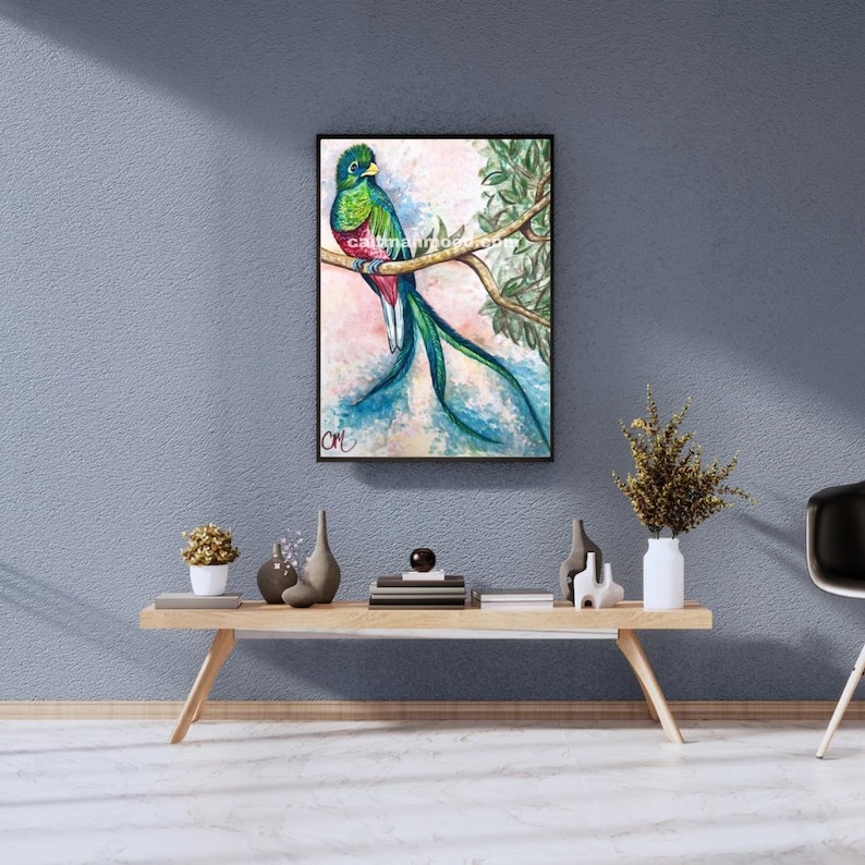 May include: A framed watercolor painting of a resplendent quetzal bird perched on a branch. The bird features green, red, and blue plumage with long tail feathers. The background has soft pink and blue hues, with green foliage.