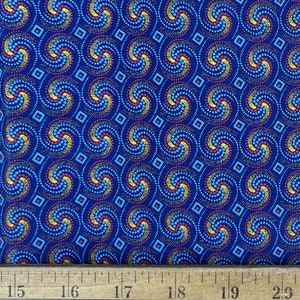 May include: Blue fabric with a repeating pattern of swirling blue, yellow, and red dots. The pattern is set against a background of small blue squares. A ruler is visible at the bottom of the image.