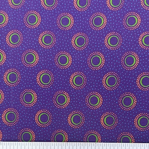 May include: Purple fabric with a repeating pattern of concentric circles. Each circle has a green center, surrounded by a ring of orange dots, and a purple outer ring. Small blue dots fill the background.