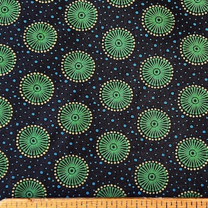 May include: Black fabric with a repeating pattern of green and yellow circles. The circles have a sunburst design. The fabric is measured with a ruler.