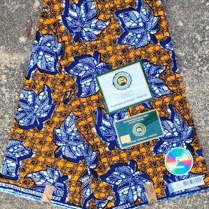 May include: A close-up of a fabric with a blue and white leaf pattern on a yellow background. The fabric is labeled "Phoenix Hitarget Printed" and "Guaranteed Real Wax Block Prints".