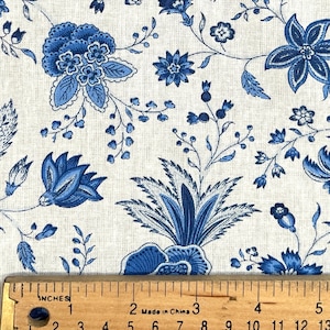 May include: White fabric with a blue floral pattern. The fabric features a repeating design of blue flowers and leaves on a white background. A ruler is placed on the fabric to show the scale.