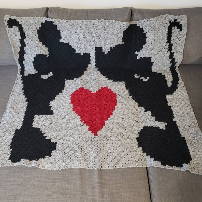 Puede incluir: Una manta de crochet gris y negro con dos siluetas de ratones bes&aacute;ndose y un coraz&oacute;n rojo en el centro.