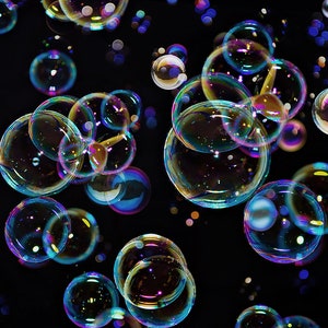 May include: A collection of iridescent soap bubbles floating against a black background. The bubbles vary in size and reflect a spectrum of colors, including blue, green, yellow, and purple. Some bubbles are clustered together, while others float independently.