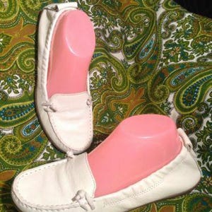May include: Pair of white leather loafers with a simple design. The loafers have a rounded toe and a flat sole.