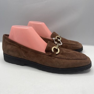 May include: Brown suede loafers with a gold chain detail. The loafers have a rounded toe and a black rubber sole.