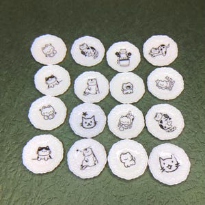 May include: A collection of sixteen small, white, round decorative plates with scalloped edges. Each plate features a different black and white cartoon cat design. The cats are in various poses, adding a playful touch to the collection.