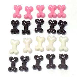 May include: An assortment of bone-shaped candies in pink, dark brown, off-white, and chocolate brown. The candies are arranged in rows on a white surface. These could be used as cake decorations or party favors.