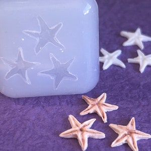 May include: A silicone mold with four starfish shapes, and five starfish made of a beige material. The mold and starfish are on a purple surface.