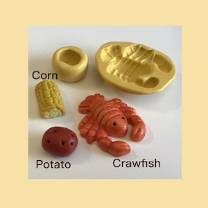 May include: A set of four silicone molds for making miniature food items. The molds are yellow and feature a crawfish, corn on the cob, a potato, and a small bowl. The molds are on a white surface.